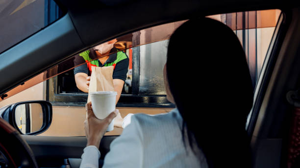 hand man in car receiving coffee in drive thru fast food restaurant. staff serving takeaway order for driver in delivery window. drive through and takeaway for buy fast food for protect covid19. - 24252 imagens e fotografias de stock