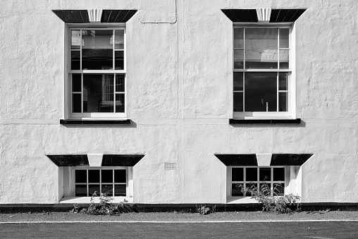 Monochrome view of a large terraced house showing the sub basement windows seen at pavement level.  Used as. holiday let on the Suffolk, UK coast.