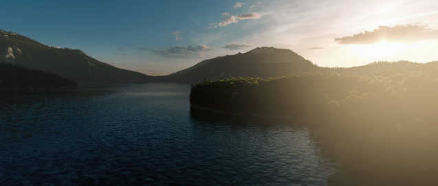 Misty mountain lake surrounded by forested mountains at sunrise.