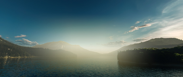 Misty mountain lake surrounded by forested mountains at sunrise.