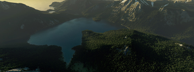 Misty mountain lake surrounded by forested mountains at sunrise. High angle view.