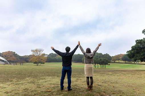 Couple standing in public park, raising hands