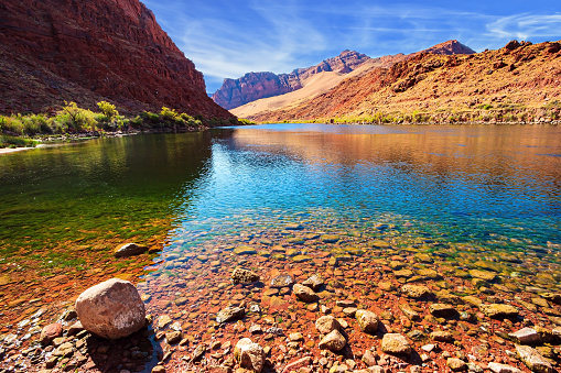 The water of the river reflects the steep rocks. The historic Lees Ferry on the Colorado River. The multicolored canyon of orange and red Navajo sandstones.