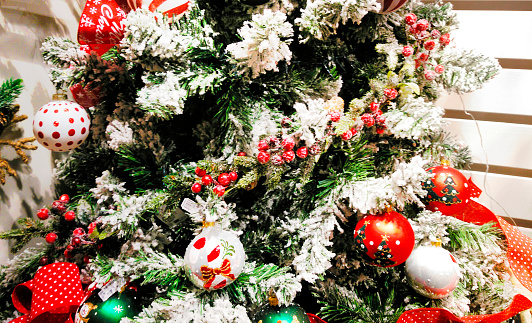 Close-up of Christmas tree with colorful ornaments in the foreground and Christmas decoration blurred in the background