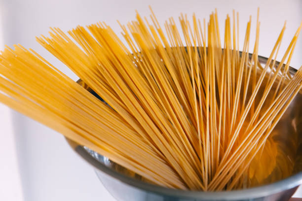 istock raw spaghetti in a metal bowl on white background. 1814858501