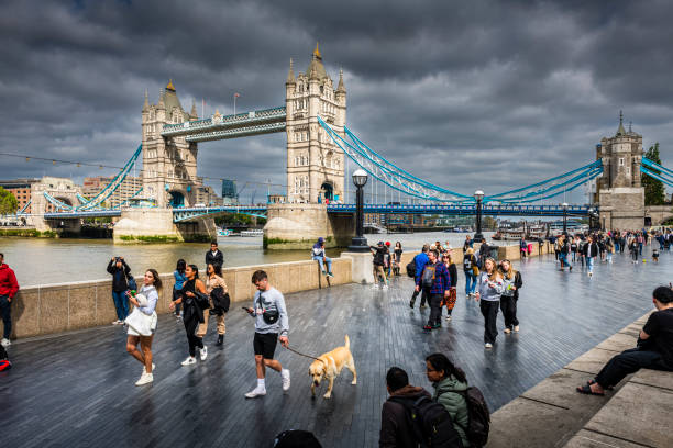London, United Kingdom - May 30, 2023:  People walking along Thames River. In background is the famous Tower Bridge.