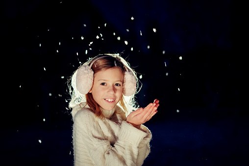 A young blonde woman in white winter clothes looks at white flying swans in the sky in the background and smiles. Swan Lake.