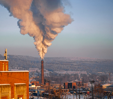 Plume of thick smoke from the pipe of an industrial heat station in the frosty Siberian air. Release of gas residues of unburned fuel from high brick pipe of power plant in the city of Ust-Kut on the Lena River.
