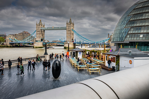 London, United Kingdom - May 30, 2023:  People walking along Thames River. In background is the famous Tower Bridge.