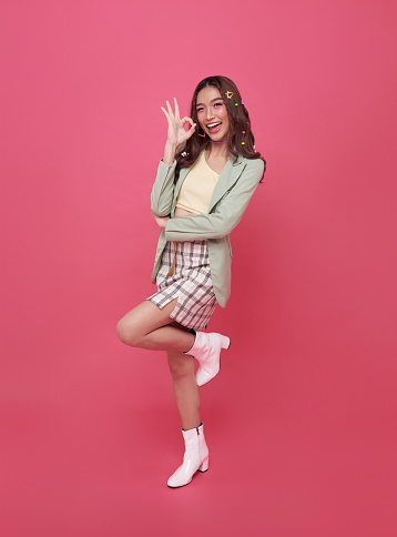 Portrait of Young beautiful Asian teen businesswoman smiling and showing ok sign on hand isolated on pink background, Looking at camera