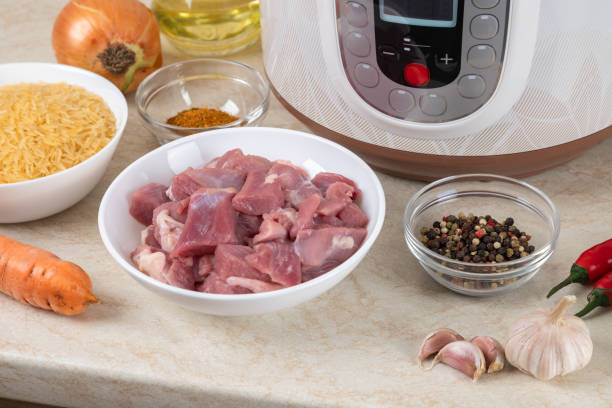 istock Prepared ingredients for cooking pilaf in modern multi cooker in kitchen on a table. Cooking pilau with meat in multicooker. 1814878170