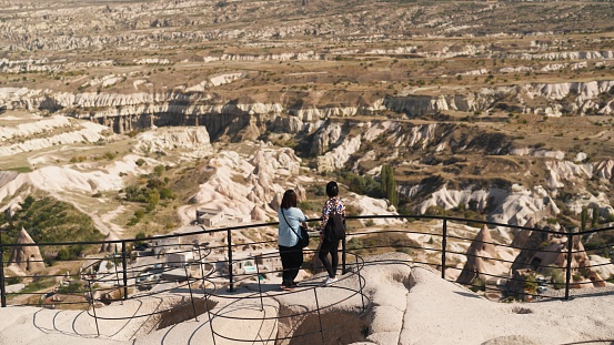 Two female tourist friends are looking at the view of Cappadocia from top of a high hill.