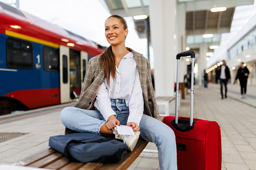 Female passenger sitting on bench at train station. Travel and active lifestyle concept. Travel by train