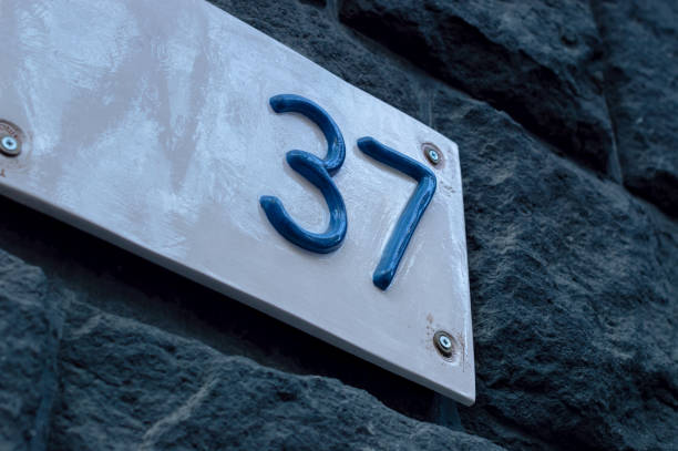 istock Number 37 building white ceramic number plate with blue numbers, on the stone bricks background 1814893900