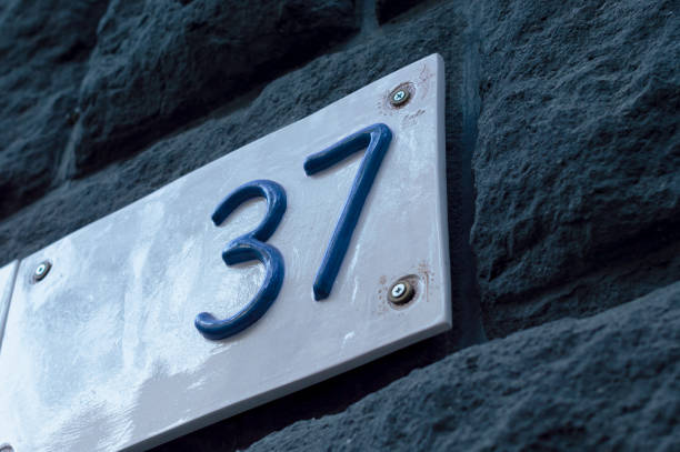 istock Number 37 building white ceramic number plate with blue numbers, on the stone bricks background 1814894982