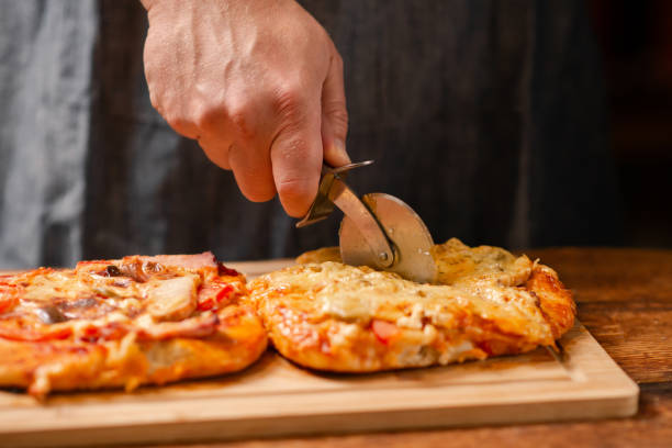 istock Pizza Crafting: A man skillfully cuts a homemade pizza on a wooden board with a specialized pizza knife 1814904584
