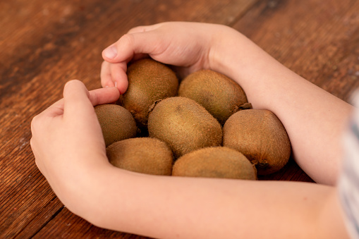 Fruitful discovery: a child cradles several whole kiwis, illustrating the nutritional value and joy of savoring these delightful fruits