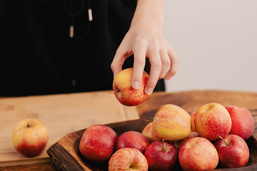 Female hands arrange a selection of ripe red apples on a wooden board, symbolizing the nourishing choices of a healthy lifestyle, vegetarian values, and the benefits of fruit
