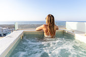 Rear view of woman relaxing in a private Hot tub outdoors at sunset