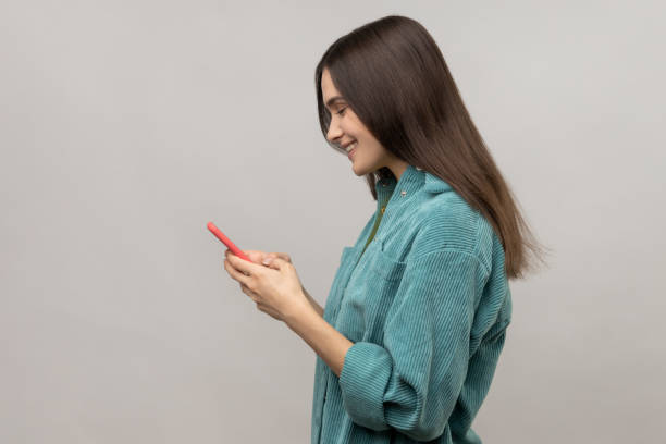 Side view of happy woman reading message on smartphone and smiling, using mobile device. stock photo