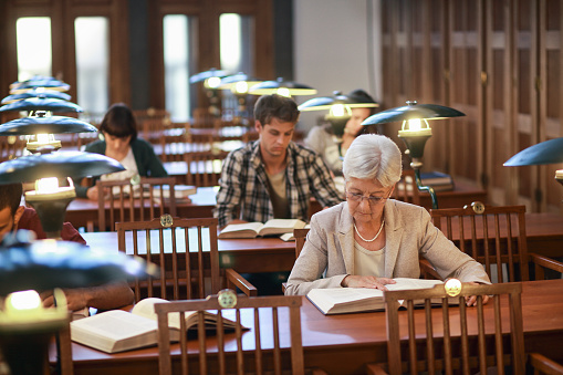 People studying in a library reading room. Old books, glasses on tables, electric lamps for lightning.