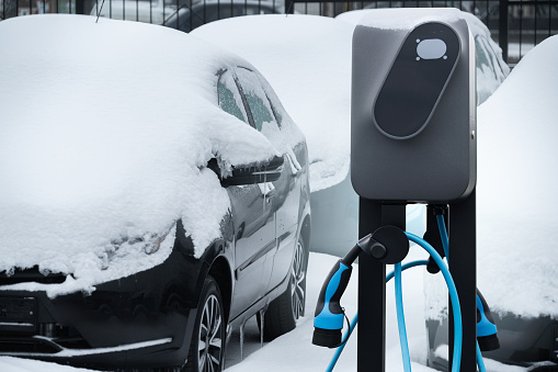 Electric car charging station on a background of snow covered winter cars.