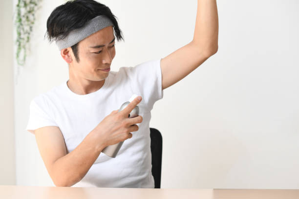 Young Asian man applying antiperspirant spray (deodorant) to his armpits