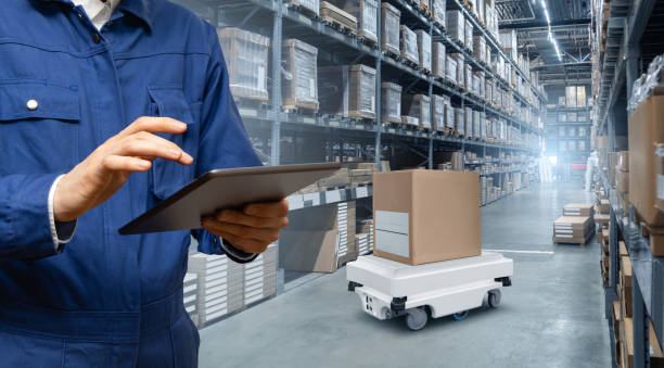 Warehouse manager with digital tablet controls robot with a package. Unmanned delivery concept