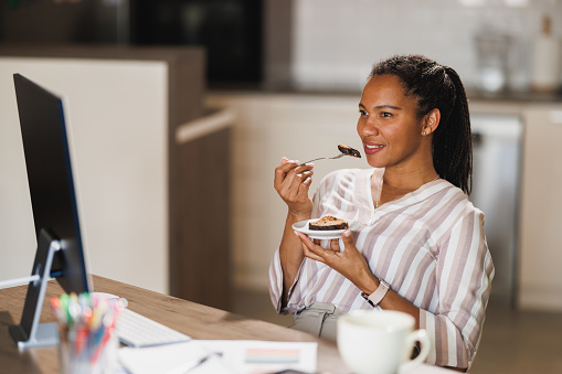 African business woman taking a break and eating chocolate cake while working at home.