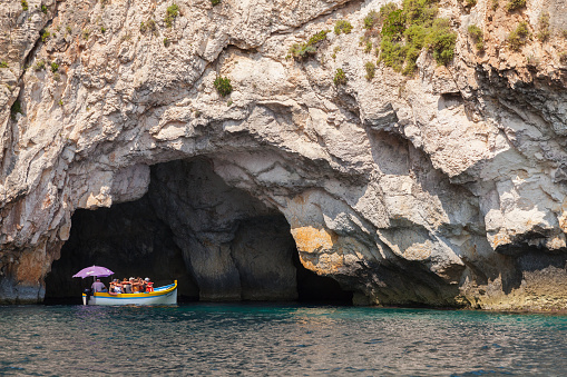 Blue Grotto, Malta - August 22, 2019: Coastal landscape with rocks and pleasure motor boat full of tourists sailing caves on a  sunny summer day