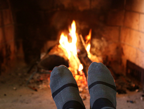 person's feet by campfire (socks on foot, warming by fire in fireplace) winter warmth, comfort, cozy (flames indoor, holiday)