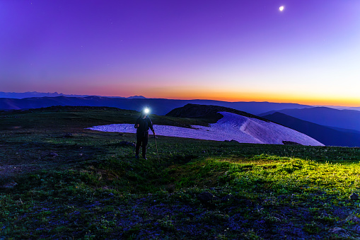 Female Hiker on Mountain Ridge Wearing Headlamp at Dusk Blue Hour - Hiking along ridge with sunset glow in sky. Hiking at high altitude using a headlamp with cool color temperature light.