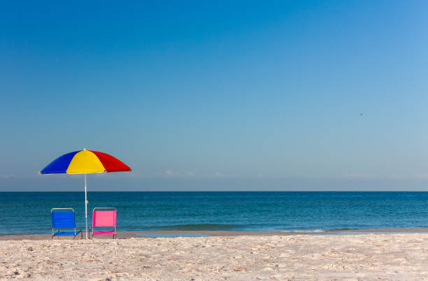 Pink and blue deck chairs on an empty beach underneath a colourful umbrella or parasol