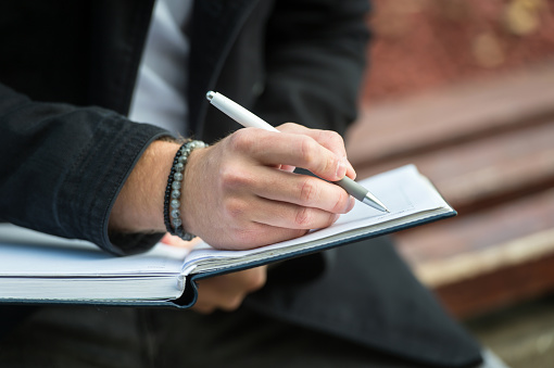 man writing on diary while sitting on a bench