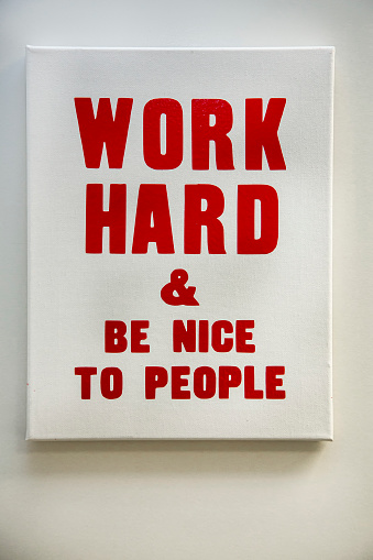 A sign in an office that states Work Hard And Be Nice To People in red letters
