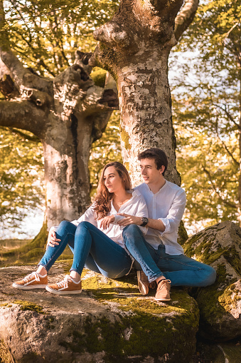 Vertical photo of a romantic scene of young couple sitting in the forest