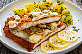 Breaded seared chicken cutlet with cheese, white mushrooms and boiled potatoes on wooden table