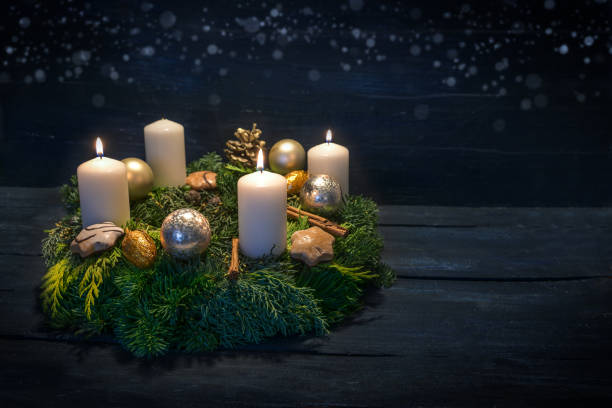 Green advent wreath with white candles, three are lit for third advent, Christmas decoration and cookies, dark blue wooden background with star bokeh, copy space