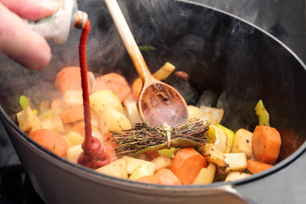 istock Tomato paste is poured into a casserole pot with steaming roasted vegetables like carrot, onion, celery, leek and a herb bouquet, cooking a sauce, stock, soup or stew, copy space 1815066705