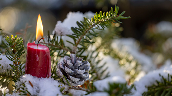 Burning candle and Christmas decoration over snow and wooden background, elegant low-key shot with festive mood