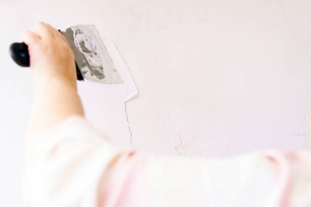 A worker seals a crack in the wall with white putty and a spatula