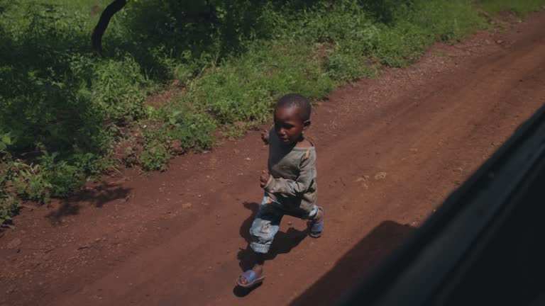 SLOW MOTION African boy running alongside a truck, african girl waving with beaming smile. Happy boys following vehicle in their village.