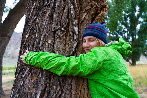 Young Environmentalist Hugging Tree - Green agenda tree hugging environmentalist hugging large tree. Female activist showing love for nature and the outdoors. Protecting Mother Gaia.