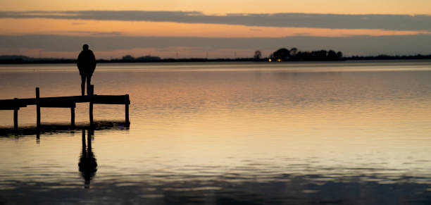 istock Rear view on Silhouette of Single man standing  on lakeside jetty at dusk 1815140846