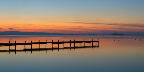 silhouette de jetée sur le lac au crépuscule avec réflexion de la rémanence à la surface de l’eau - steinhuder meer photos et images de collection