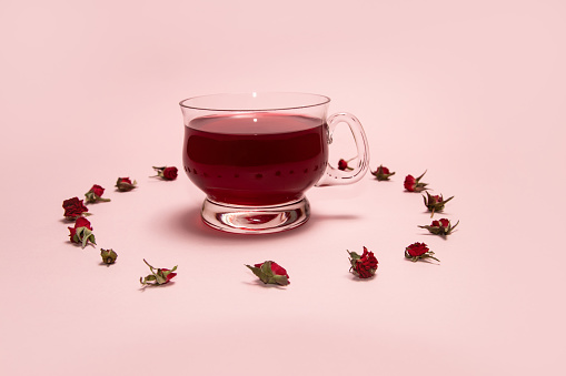 A circle of red rosebuds around herbal tea in a glass cup