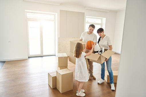 People unpack things in a new house, a girl takes a ball out of a box