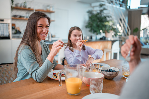 In their home dining room, a multigeneration Caucasian family shares a delightful meal, relishing waffles topped with blueberries and raspberries.