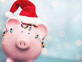 Piggy bank wrapped in tiny Christmas lights wearing a Santa hat. Holiday savings