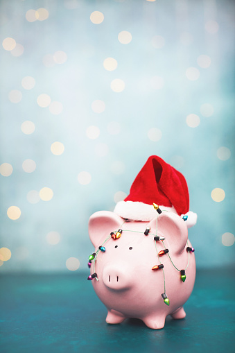 Piggy bank wrapped in tiny Christmas lights wearing a Santa hat. Holiday savings. Shot with copy space